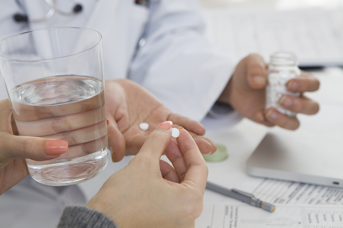 a woman holds a glass of water and a pill as she asks what is medication assisted treatment