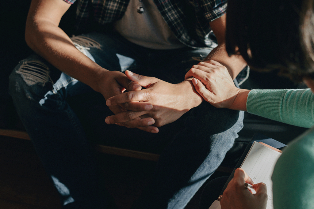 person with hands clasped is comforted by a friend while considering dual diagnosis treatment