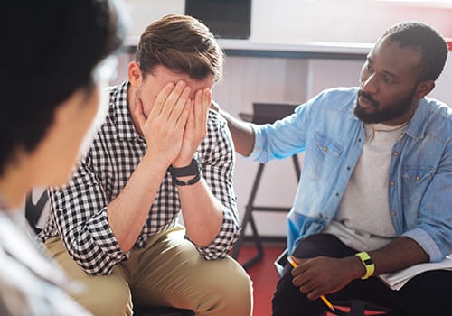 group of men and women participating in a dual diagnosis treatment program where one man is consoling another